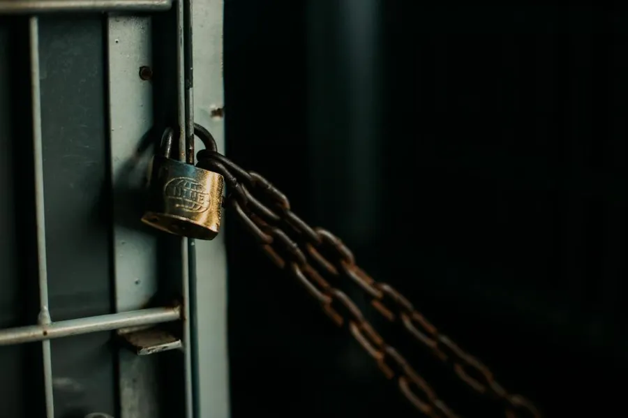 A brass padlock and chain on a metal gate
