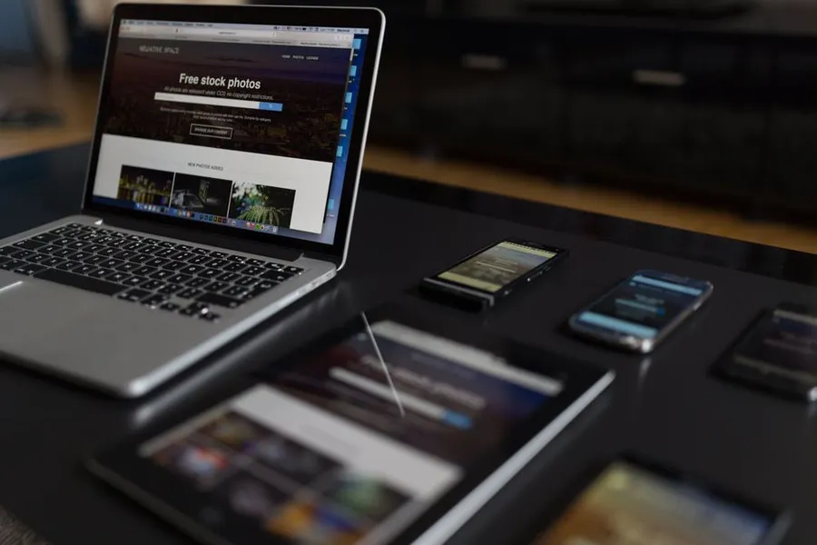 A laptop, tablet and phones on a dark desk